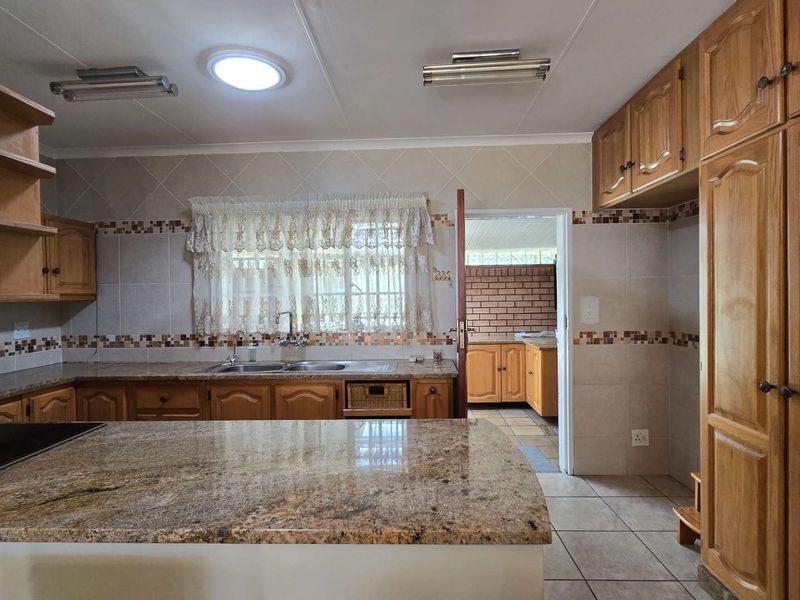 Spacious kitchen featuring granite countertops, extensive wooden cabinetry, and tiled finishes, with an adjoining scullery area visible through the doorway.