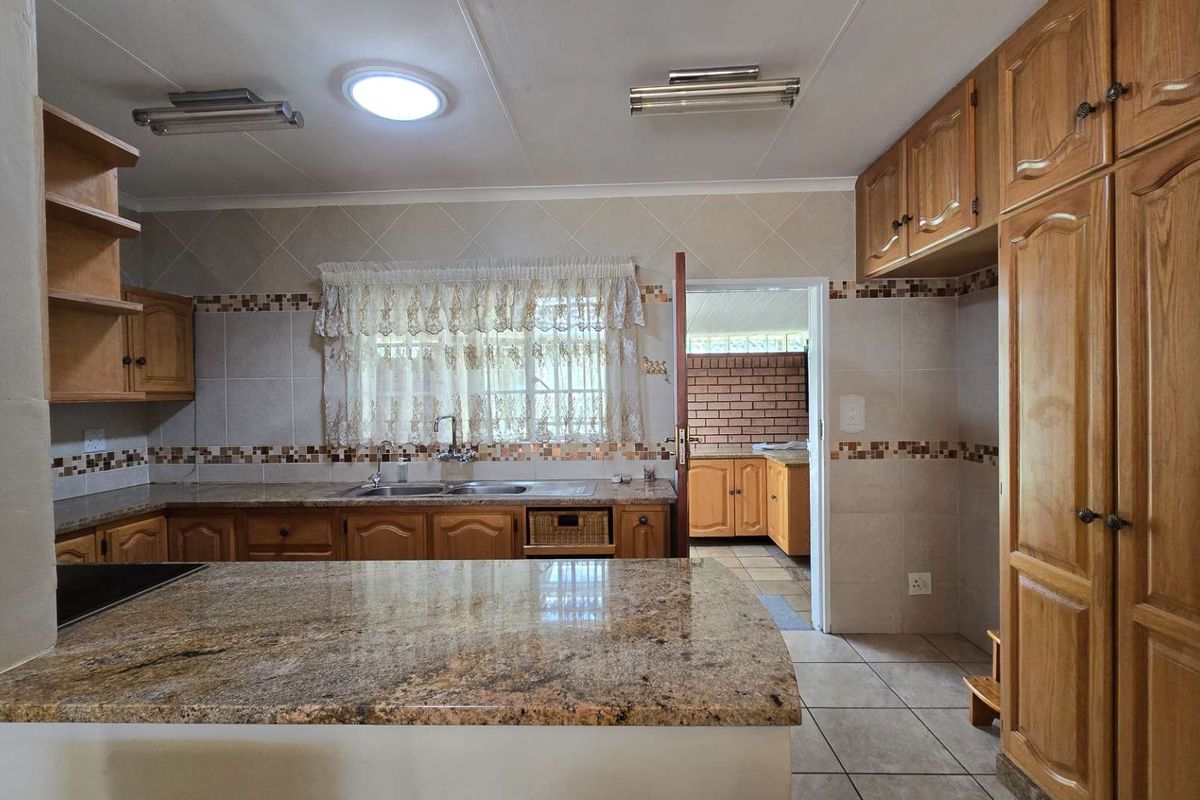 Spacious kitchen featuring granite countertops, extensive wooden cabinetry, and tiled finishes, with an adjoining scullery area visible through the doorway.