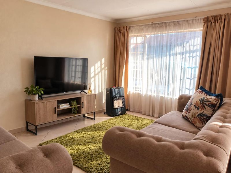 A well-lit living room featuring tiled flooring, neutral wall finishes, and large windows with curtain tracks, creating a comfortable and inviting space.