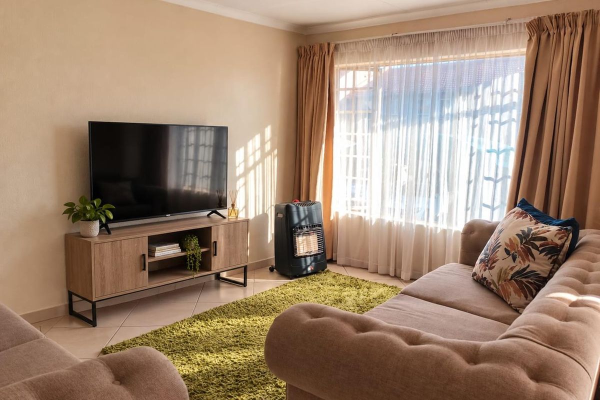 A well-lit living room featuring tiled flooring, neutral wall finishes, and large windows with curtain tracks, creating a comfortable and inviting space.