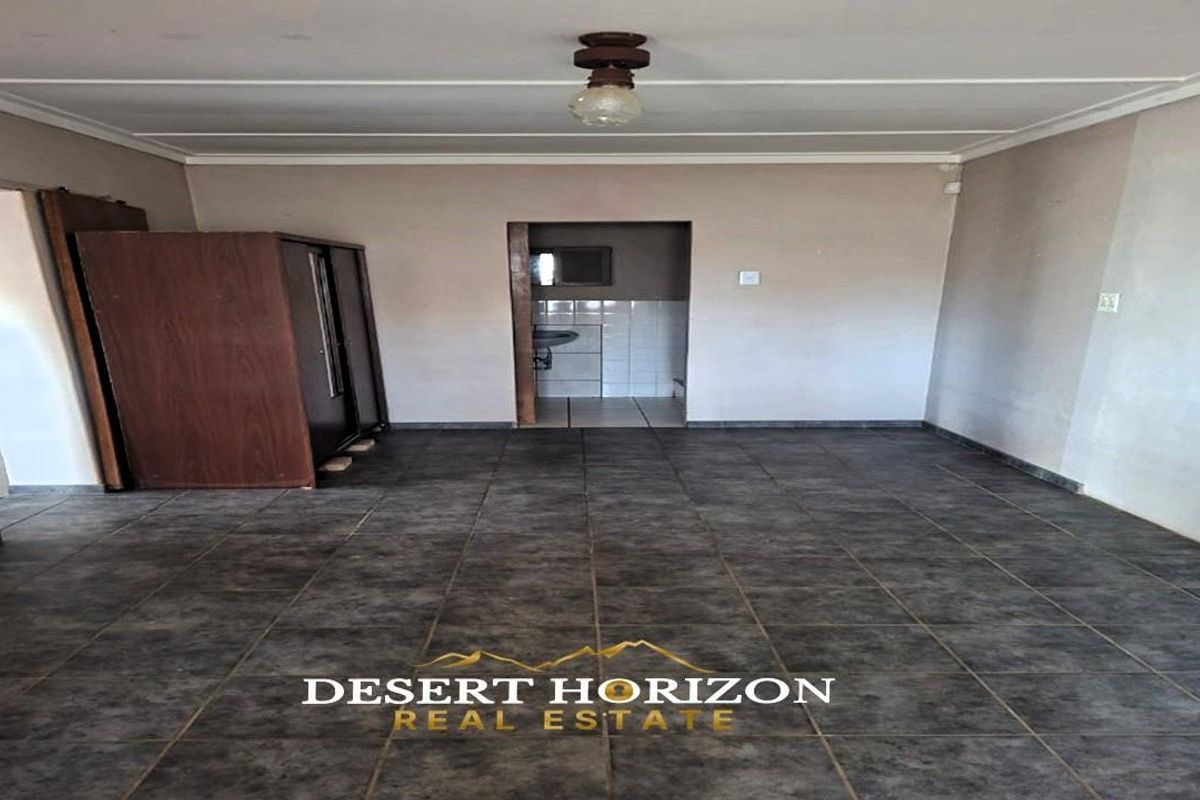 An empty living area featuring dark tiled flooring and a simple ceiling light fixture, with an adjacent view into a tiled utility or bathroom space.