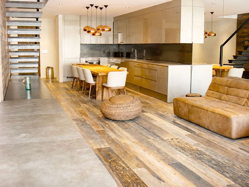 Modern open-plan living and kitchen area featuring high-end cabinetry, integrated appliances, mixed flooring materials, and a striking architectural staircase.