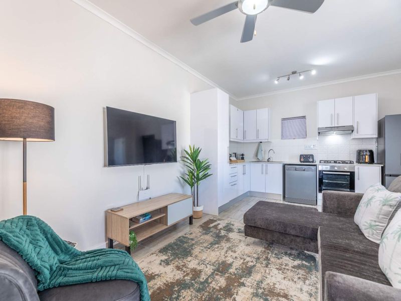 An open-plan living area featuring a modern kitchen with built-in cabinetry, stainless steel appliances, and tiled flooring, seamlessly connected to the lounge space.