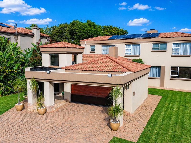 Aerial view of a well-maintained residential property featuring a paved driveway, automated garage, and solar panels on a terracotta tiled roof.