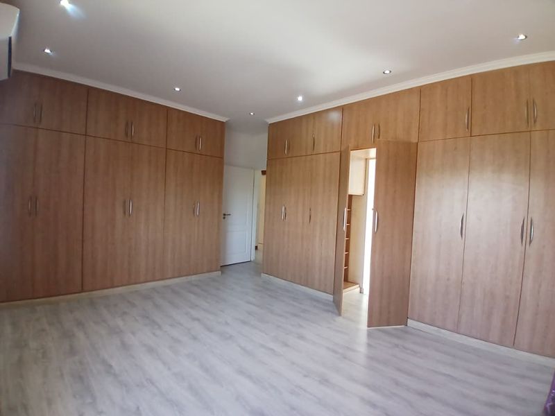 Spacious bedroom featuring extensive wall-to-wall built-in cabinetry, modern laminate flooring, and recessed ceiling downlights.