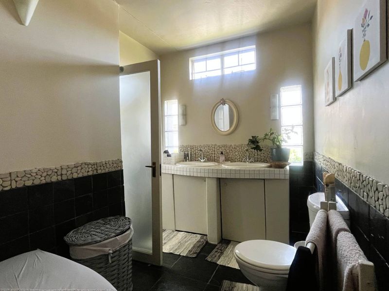 A functional bathroom featuring a double vanity with tiled countertops, built-in cabinetry, and a combination of black and pebble-style wall tiling.