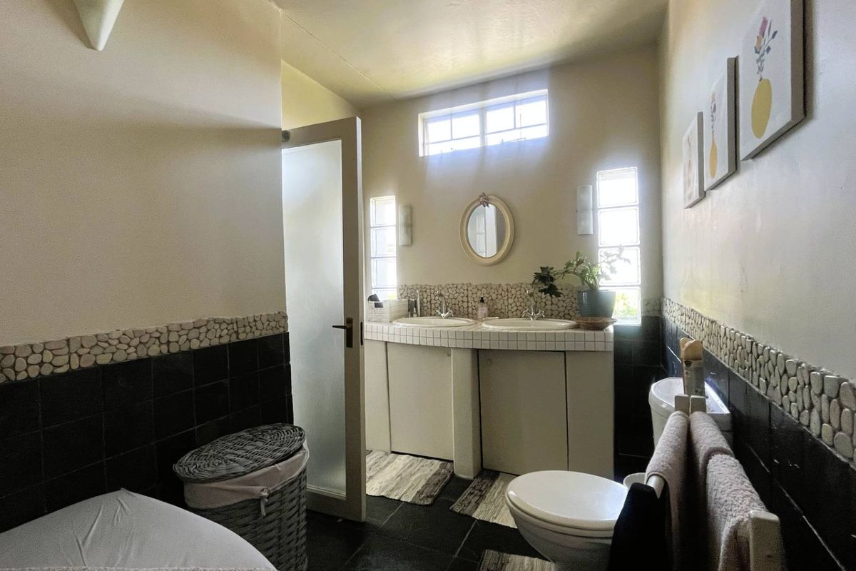 A functional bathroom featuring a double vanity with tiled countertops, built-in cabinetry, and a combination of black and pebble-style wall tiling.