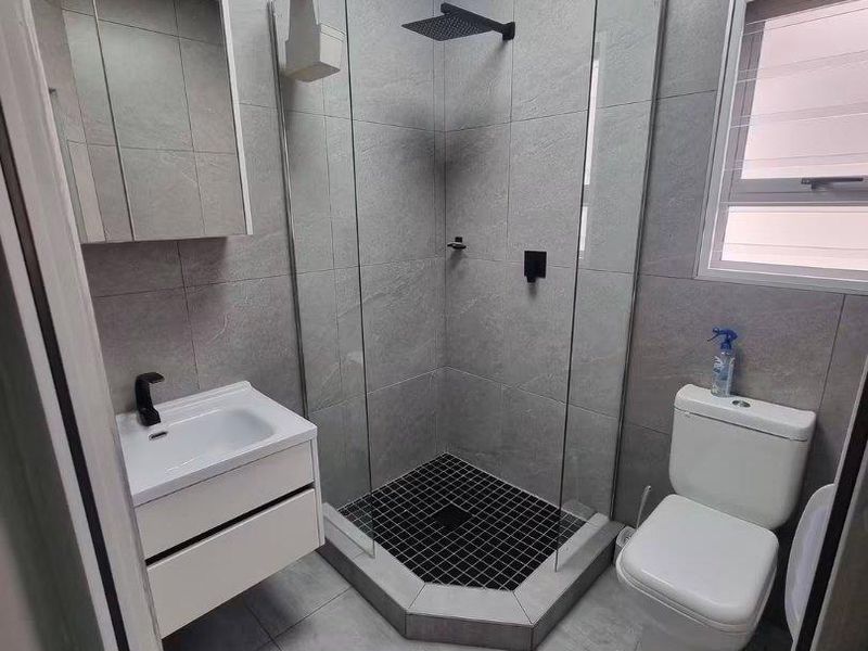 Modern bathroom featuring a walk-in shower with a rain shower head, wall-mounted vanity, and contemporary grey tiling throughout.