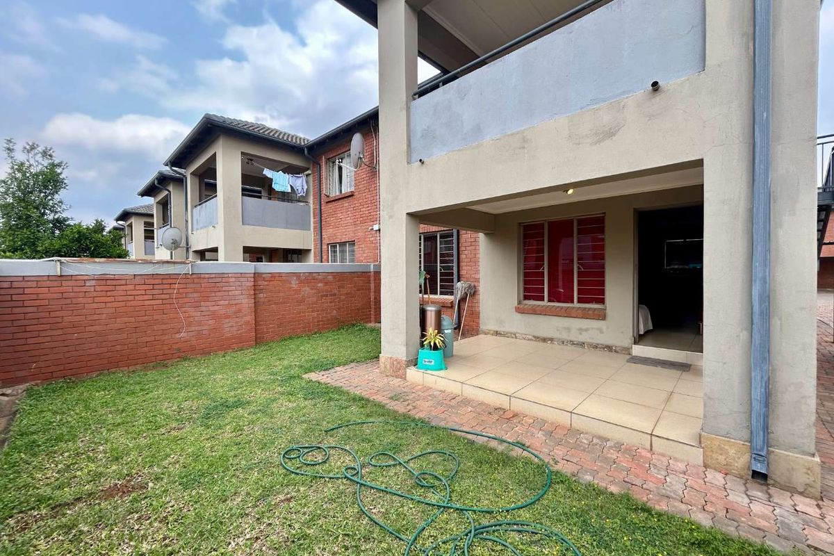 Rear view of the apartment complex featuring a private garden, paved patio area, and upper-level balcony with brick and plaster facade.