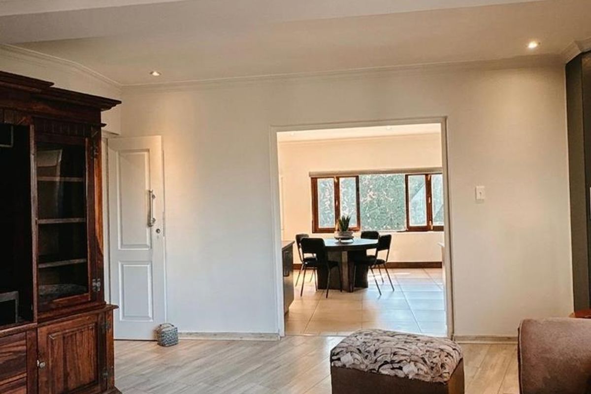 A well-maintained living room featuring laminate flooring, recessed downlighting, and decorative cove cornicing, with an open transition into the adjacent dining area.