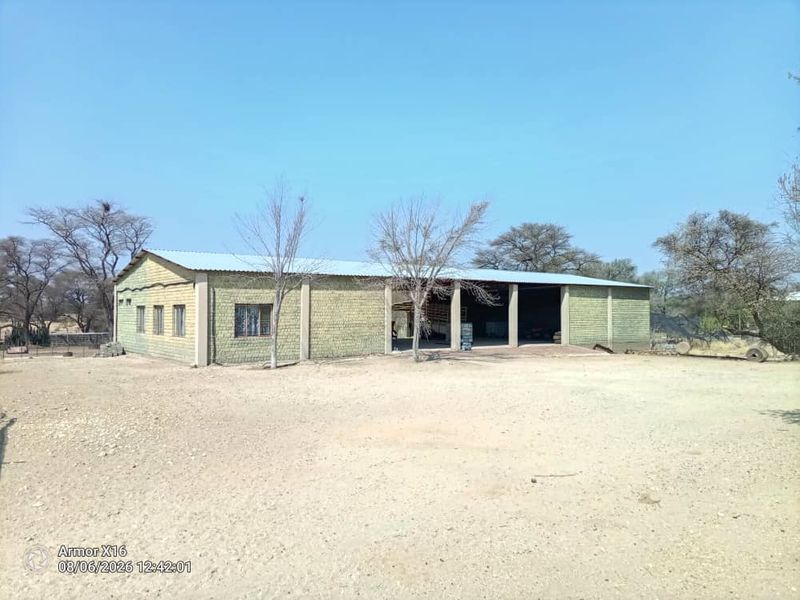 A large, utilitarian outbuilding or workshop on a small holding, featuring a corrugated metal roof and open-bay design with concrete block construction.