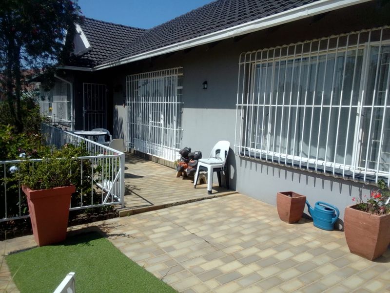 A paved outdoor patio area featuring security bars on windows and doors, overlooking a small garden space.