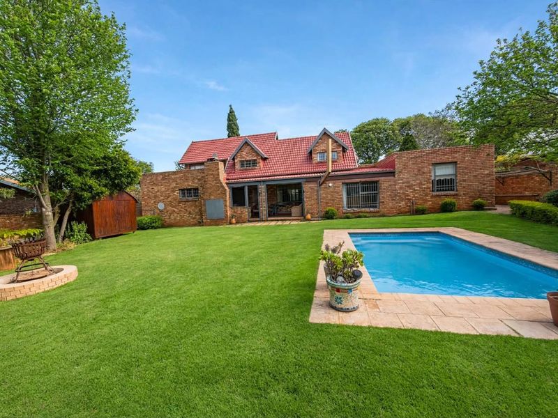 Rear view of a brick house featuring a well-maintained lawn, a swimming pool with paved surround, and a tiled roof.