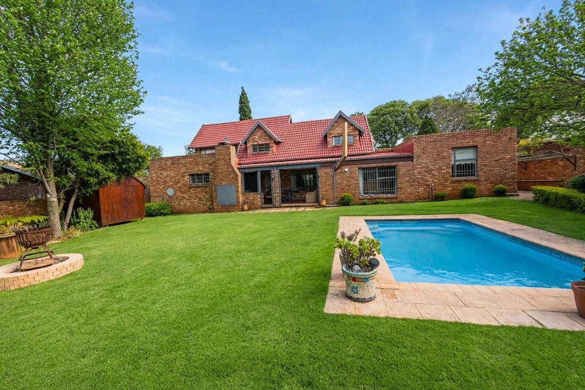 Rear view of a brick house featuring a well-maintained lawn, a swimming pool with paved surround, and a tiled roof.