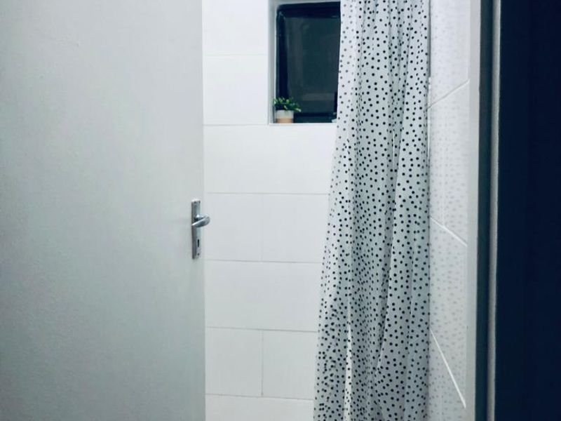 A functional bathroom shower area featuring white wall tiles, hexagonal floor tiling, and a wall-mounted shower head.