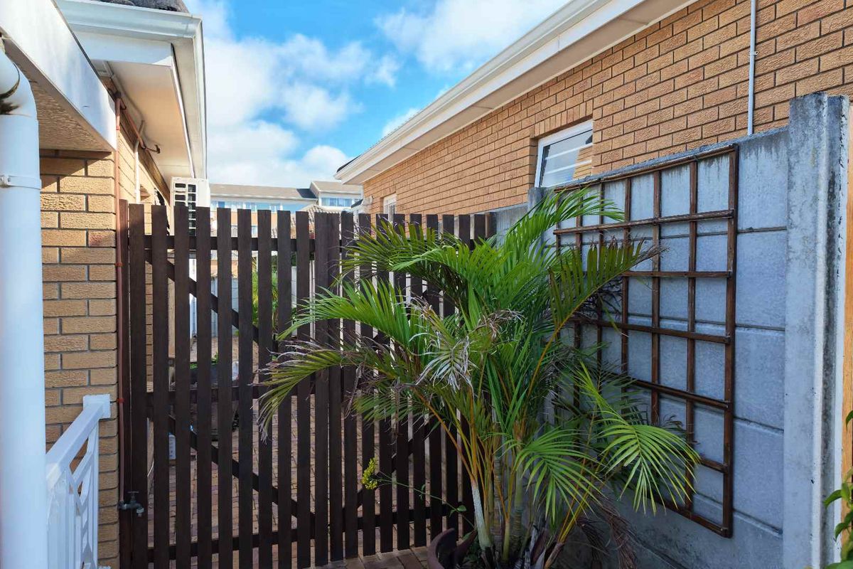 A side passage area featuring a timber gate, brick exterior walls, and a concrete boundary wall with a trellis.