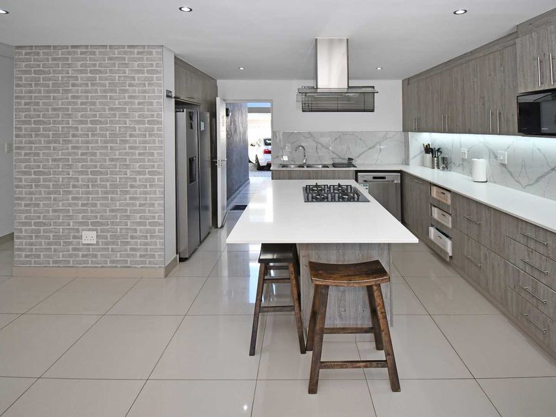 Modern kitchen featuring a central island, stone countertops, wood-finish cabinetry, built-in appliances, and sleek tiled flooring with recessed lighting.