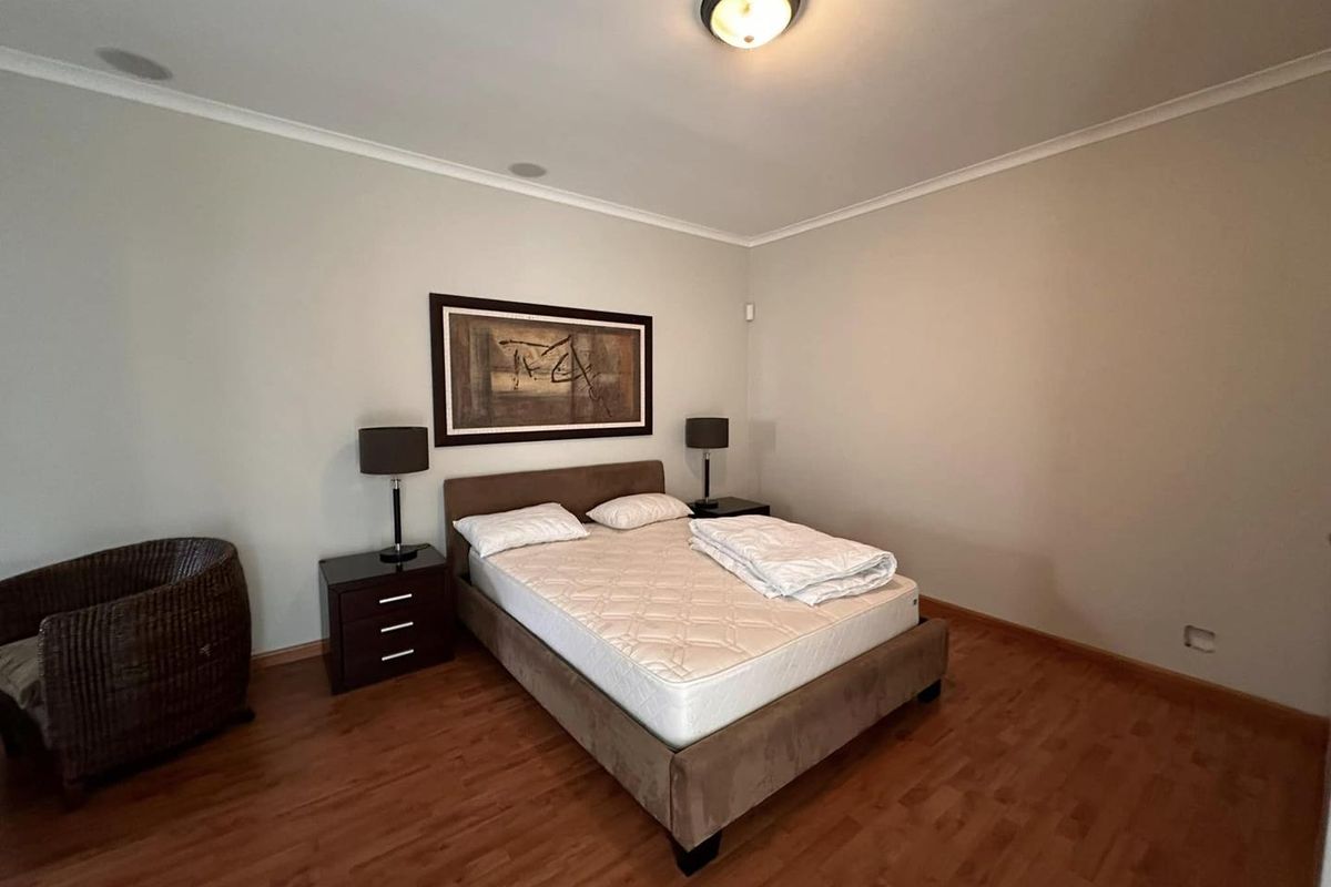 A spacious bedroom featuring warm-toned laminate flooring, neutral wall finishes, and a central ceiling light fixture.