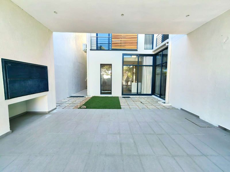 A modern covered patio featuring a built-in braai, tiled flooring, and direct access to the interior through large sliding glass doors.