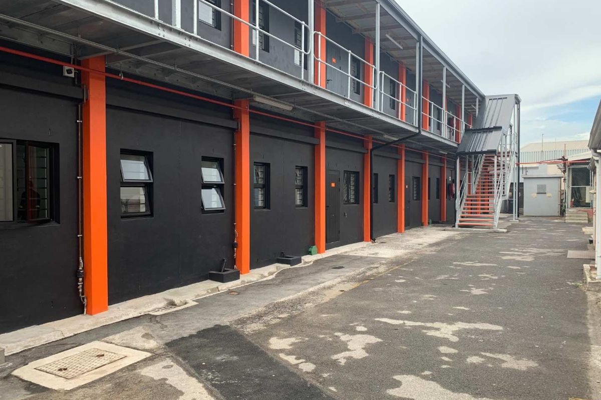 Exterior view of a modern industrial-style mixed-use building featuring black facade panels, orange structural columns, metal walkways, and an external staircase.