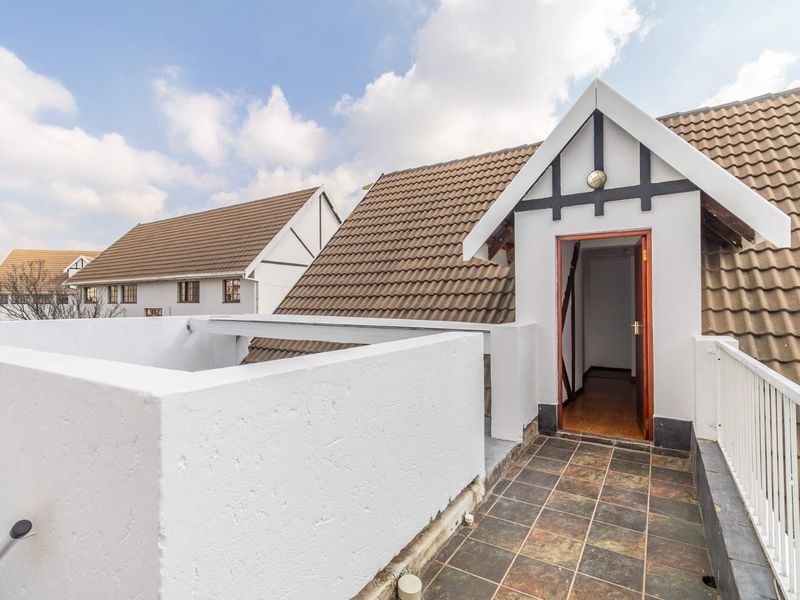 An elevated balcony area featuring tiled flooring, a white balustrade, and direct access to the interior through a timber door.