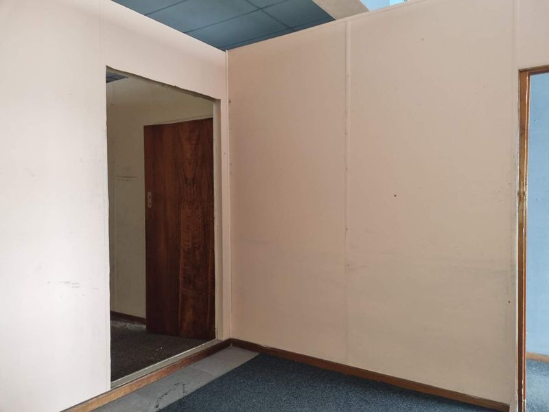 An empty office space featuring partition walls, carpet flooring, and a timber door, suitable for a professional workspace layout.
