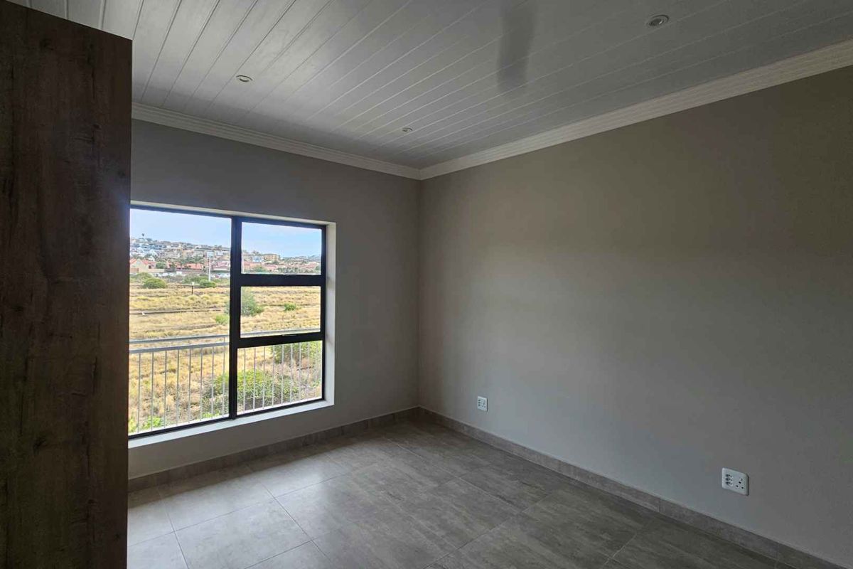 A bright, empty bedroom featuring tiled flooring, a built-in cupboard, and a large window offering scenic views.