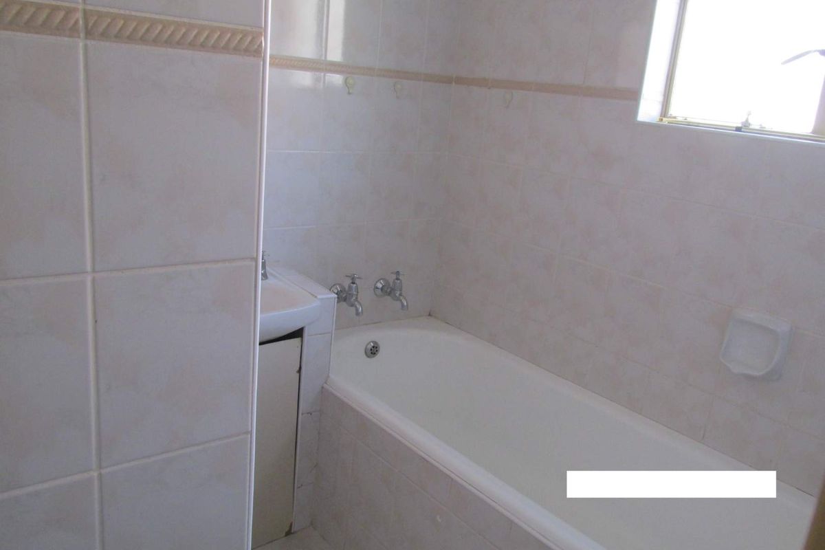 A functional bathroom featuring a built-in bathtub, wall-mounted basin, and full-height ceramic wall tiling.