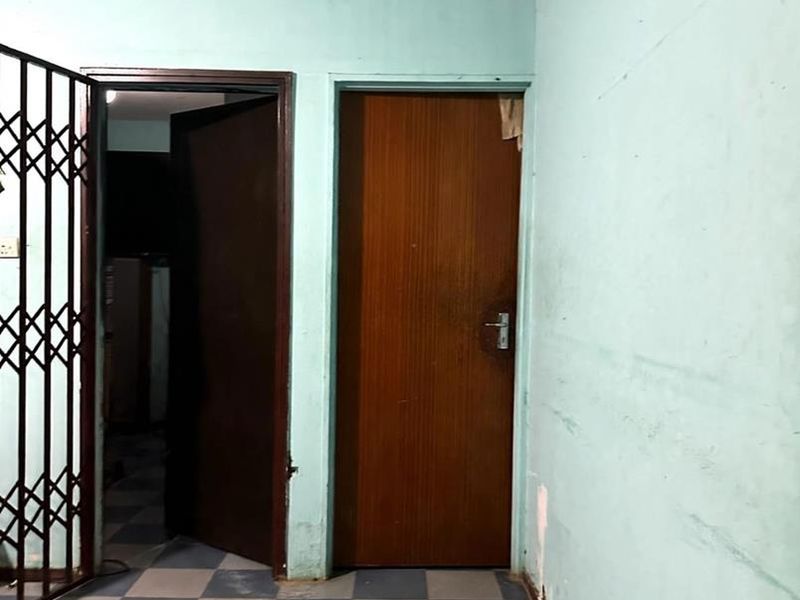A vacant hallway featuring checkered floor tiles, a security gate, and internal doors, requiring cosmetic updates to the wall finishes.