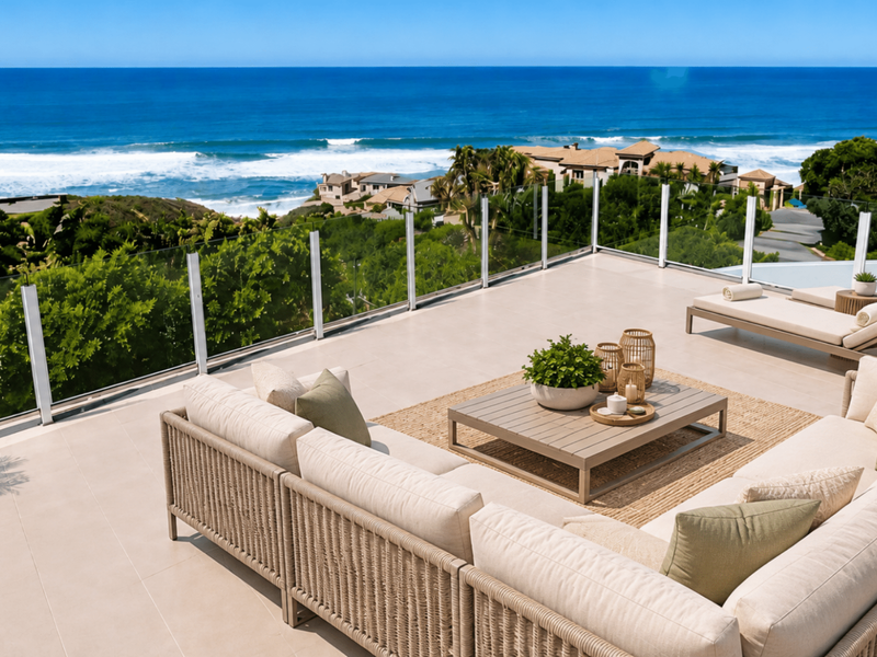 Spacious outdoor terrace featuring modern tiled flooring and a sleek glass balustrade, offering expansive, unobstructed views of the ocean and coastline.