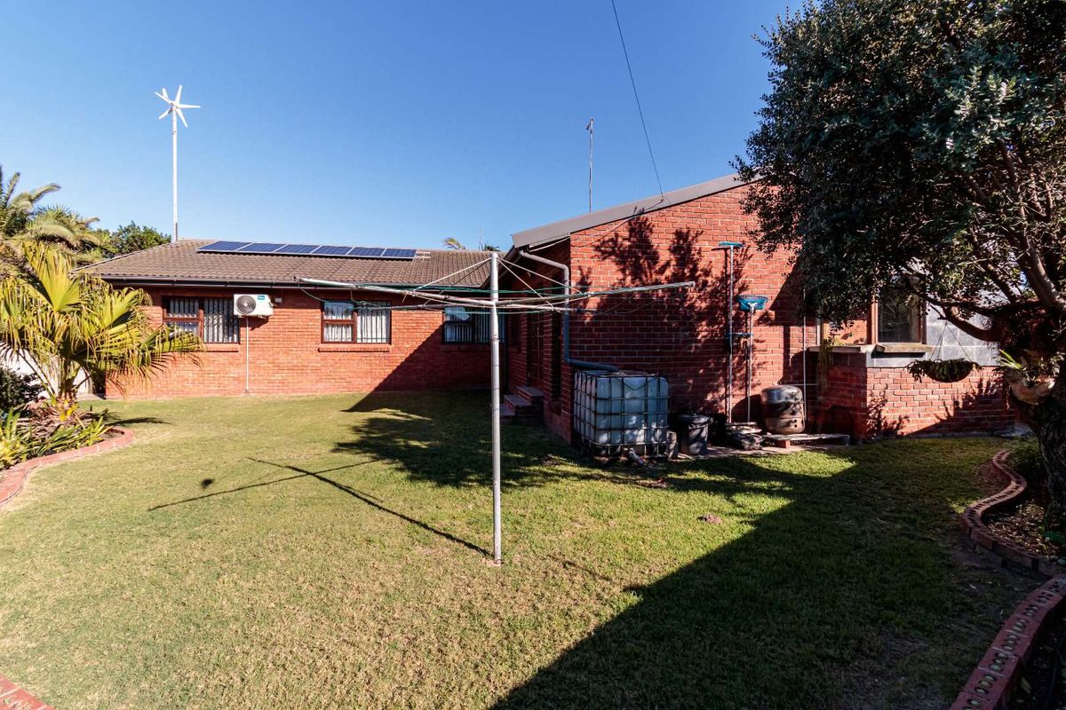 Rear view of a brick house featuring a lawn, solar panels, and an external air conditioning unit.