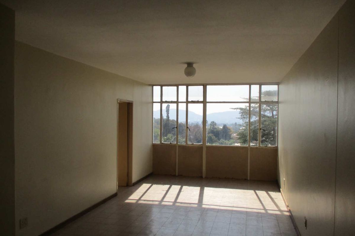 An empty, sunlit living room featuring large windows with scenic views and tiled flooring, offering a blank canvas for renovation.