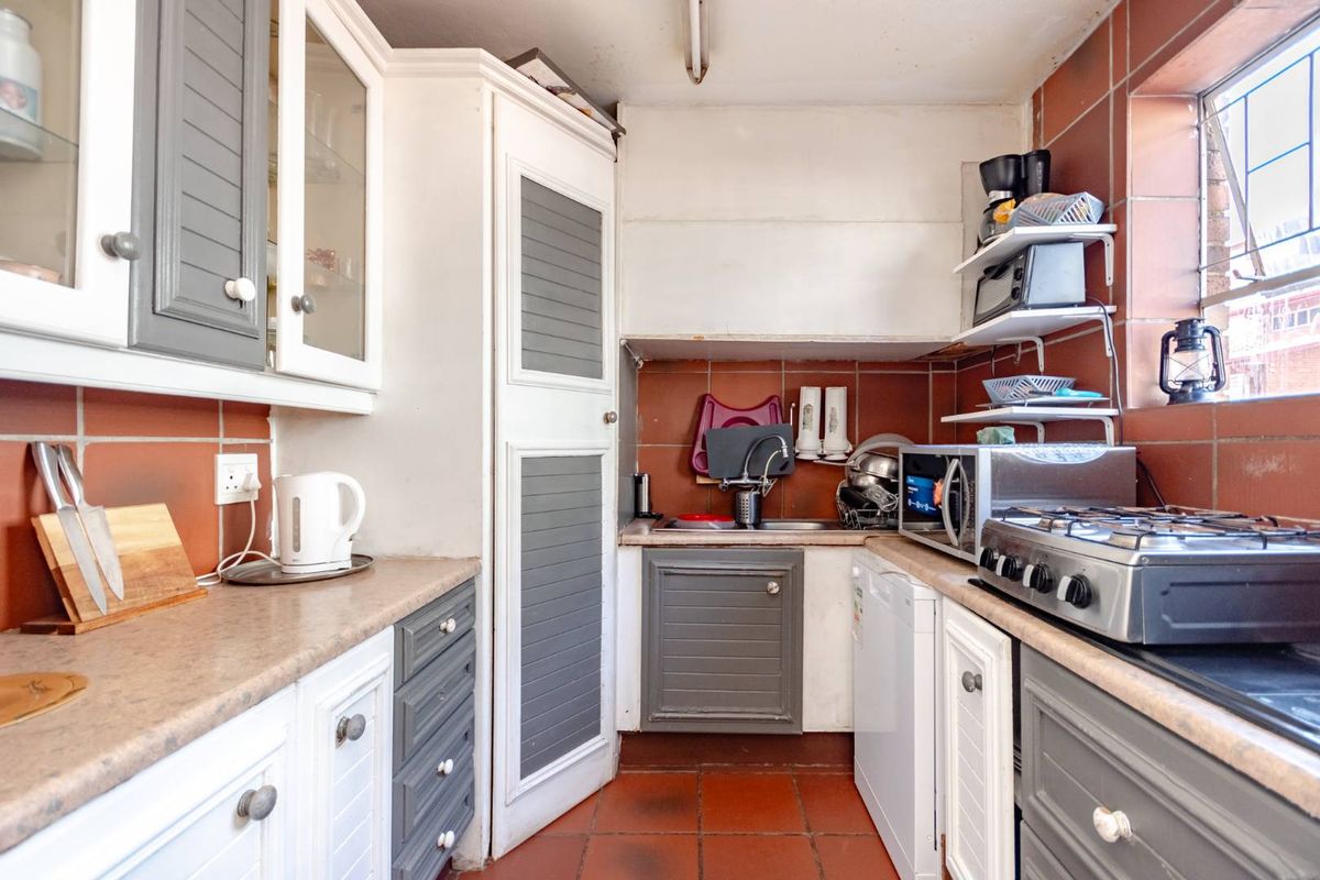 Compact kitchen featuring two-tone cabinetry, tiled splashbacks, and a gas hob, offering a functional layout in need of cosmetic updates.