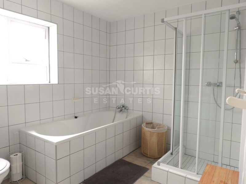 A functional bathroom featuring a built-in bathtub, separate shower enclosure, and white wall tiling throughout.