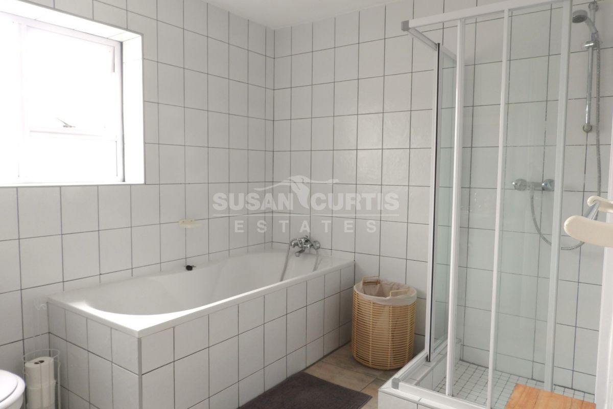 A functional bathroom featuring a built-in bathtub, separate shower enclosure, and white wall tiling throughout.
