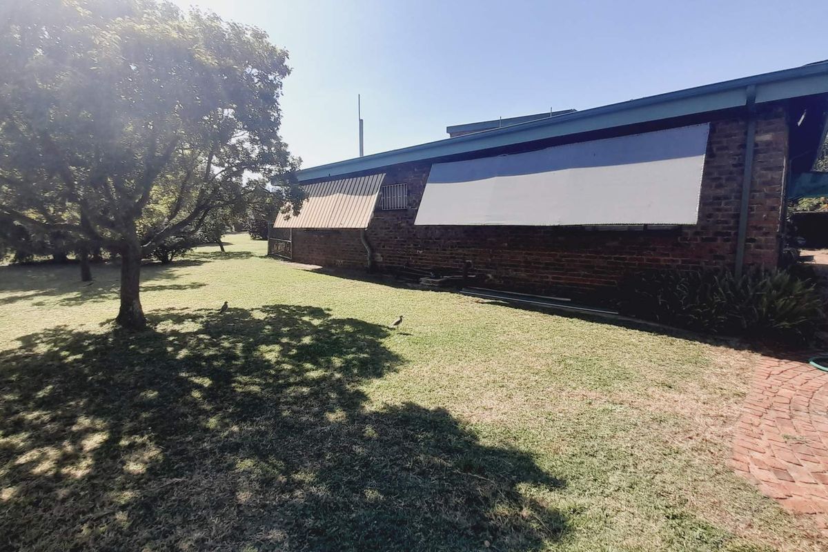 Rear view of the farm property featuring a brick exterior, retractable window awnings, and a spacious garden area with a brick paved path.