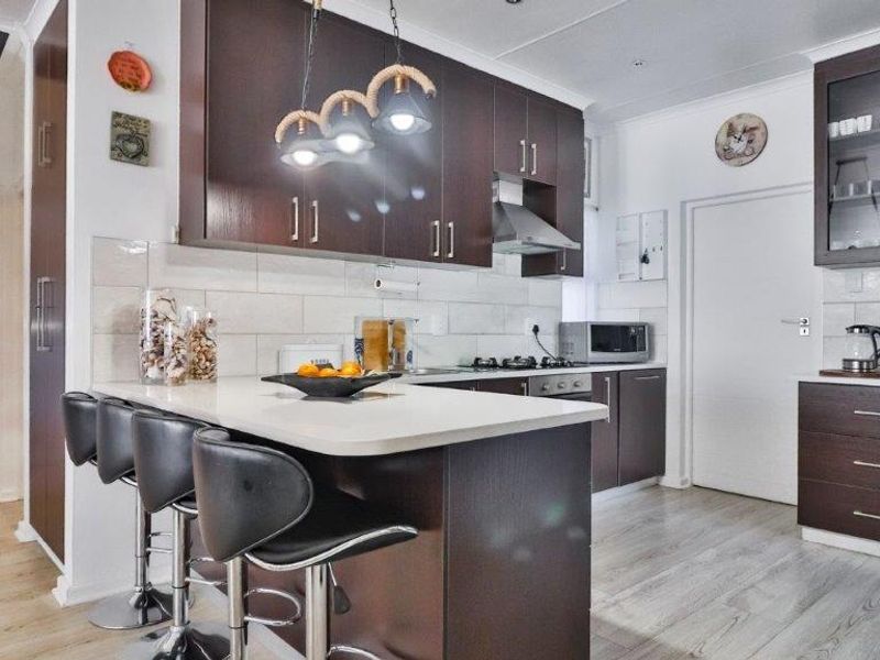 Modern kitchen featuring dark wood cabinetry, stone countertops, a breakfast bar, and a subway tile backsplash, with an open flow to the adjacent bedroom.