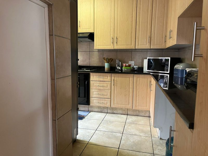 A functional kitchen featuring light wood-finish cabinetry, black granite countertops, built-in oven, hob, and extractor fan with tiled flooring and backsplash.