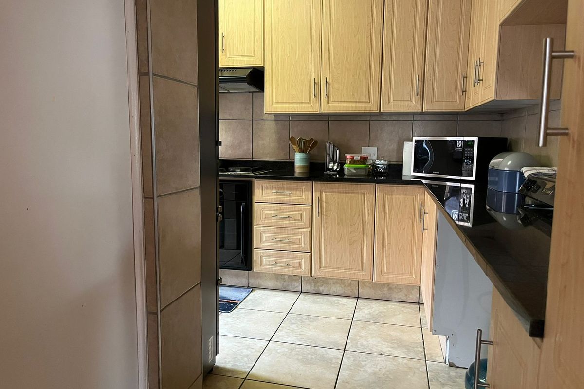 A functional kitchen featuring light wood-finish cabinetry, black granite countertops, built-in oven, hob, and extractor fan with tiled flooring and backsplash.