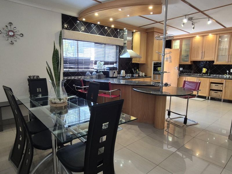 Open-plan kitchen and dining area featuring wooden cabinetry, granite countertops, tiled flooring, and integrated lighting, creating a functional and connected living space.