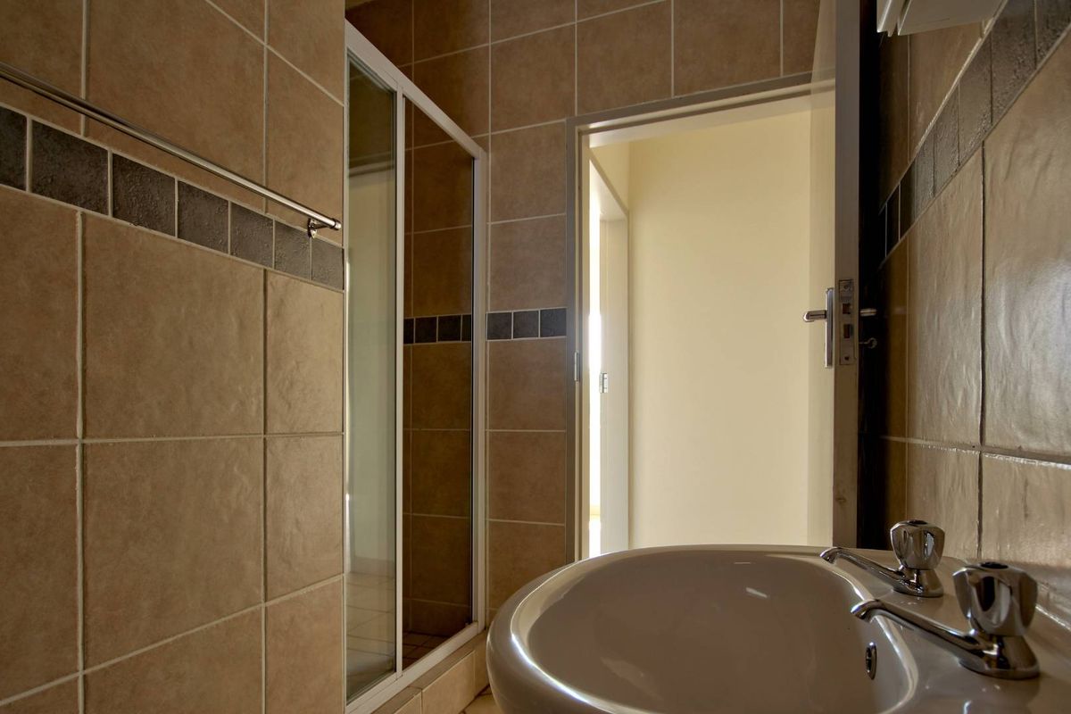 A functional bathroom featuring tiled walls, a pedestal basin with chrome taps, and a glass-enclosed shower stall.