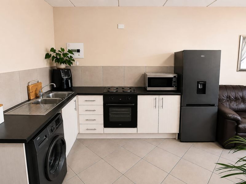 An open-plan kitchen area featuring light-toned cabinetry, dark countertops, integrated oven and hob, and tiled flooring, seamlessly connecting to the living space.