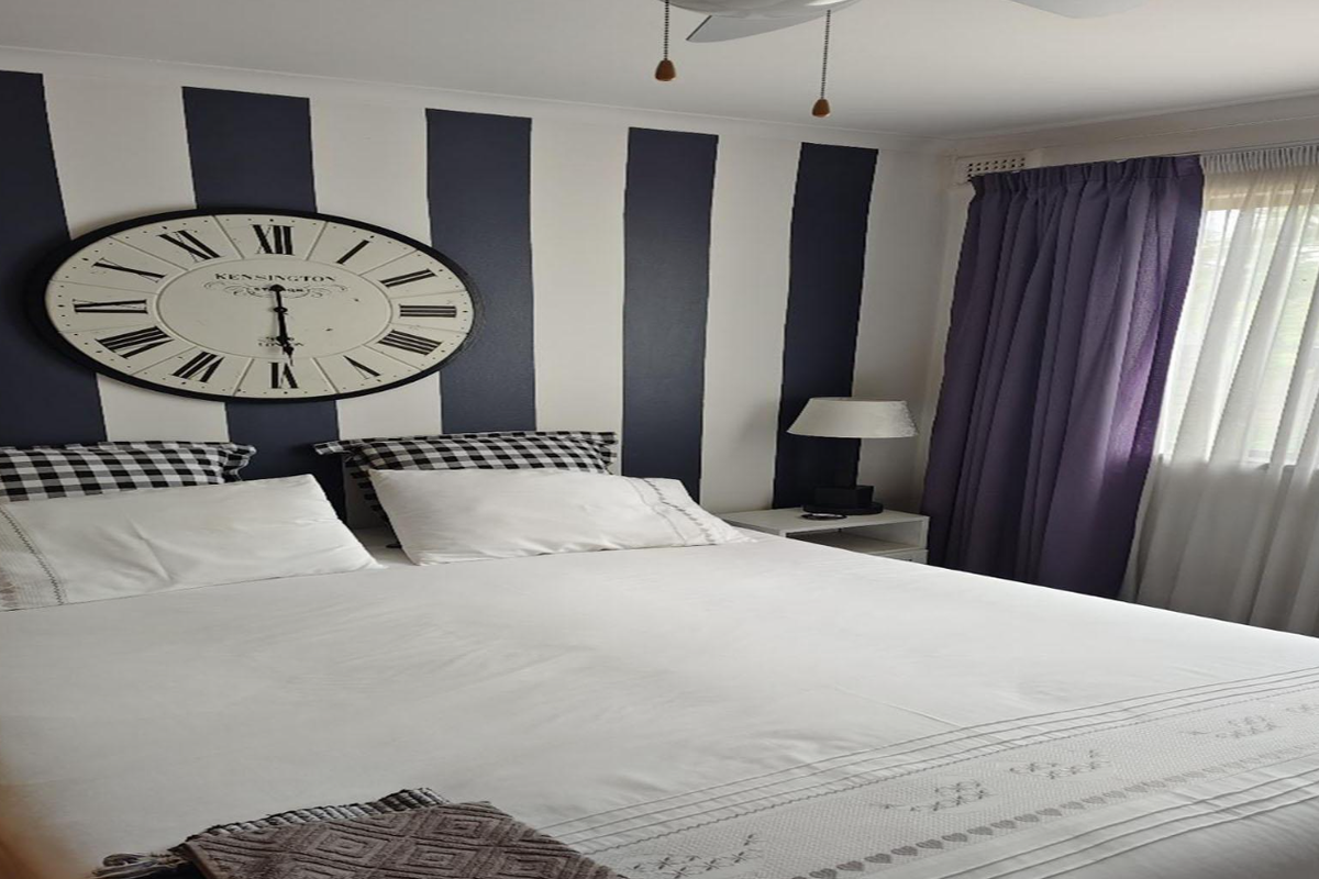 A bedroom featuring a ceiling fan and window treatments, characterized by a striped accent wall.