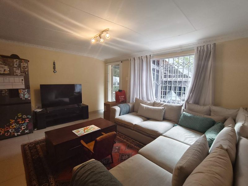 A comfortable living room featuring tiled flooring, ceiling coving, and a security gate over the window, providing a functional and secure living space.