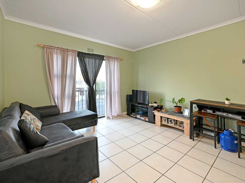 A living room featuring ceramic floor tiles, neutral green walls, and a sliding glass door providing access to a balcony.