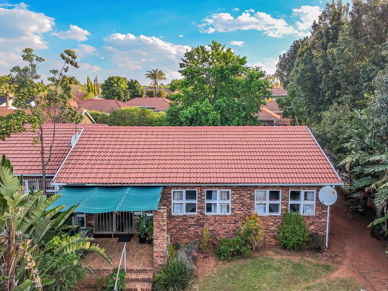 Aerial view of the rear elevation of a brick townhouse featuring a tiled roof, covered patio area, and established garden surroundings.