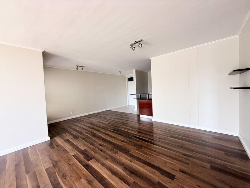 Spacious open-plan living area featuring dark laminate flooring, neutral walls, ceiling spotlights, and a built-in breakfast bar counter.