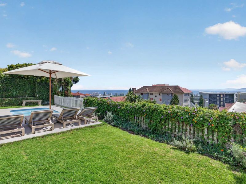 A well-maintained outdoor pool area featuring a paved deck, landscaped garden, and scenic coastal views.