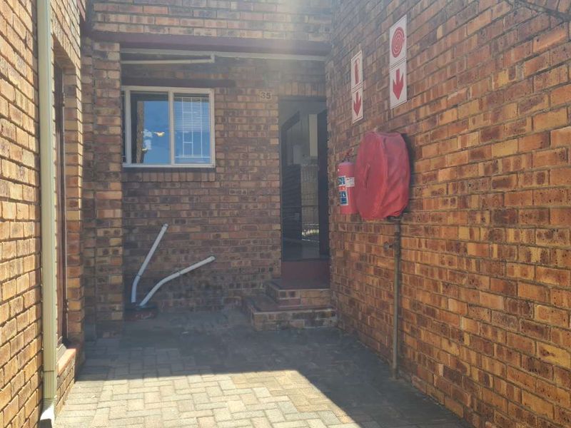 Front entrance area of the townhouse featuring face brick construction, paved flooring, and essential fire safety equipment including a hose reel and extinguisher.
