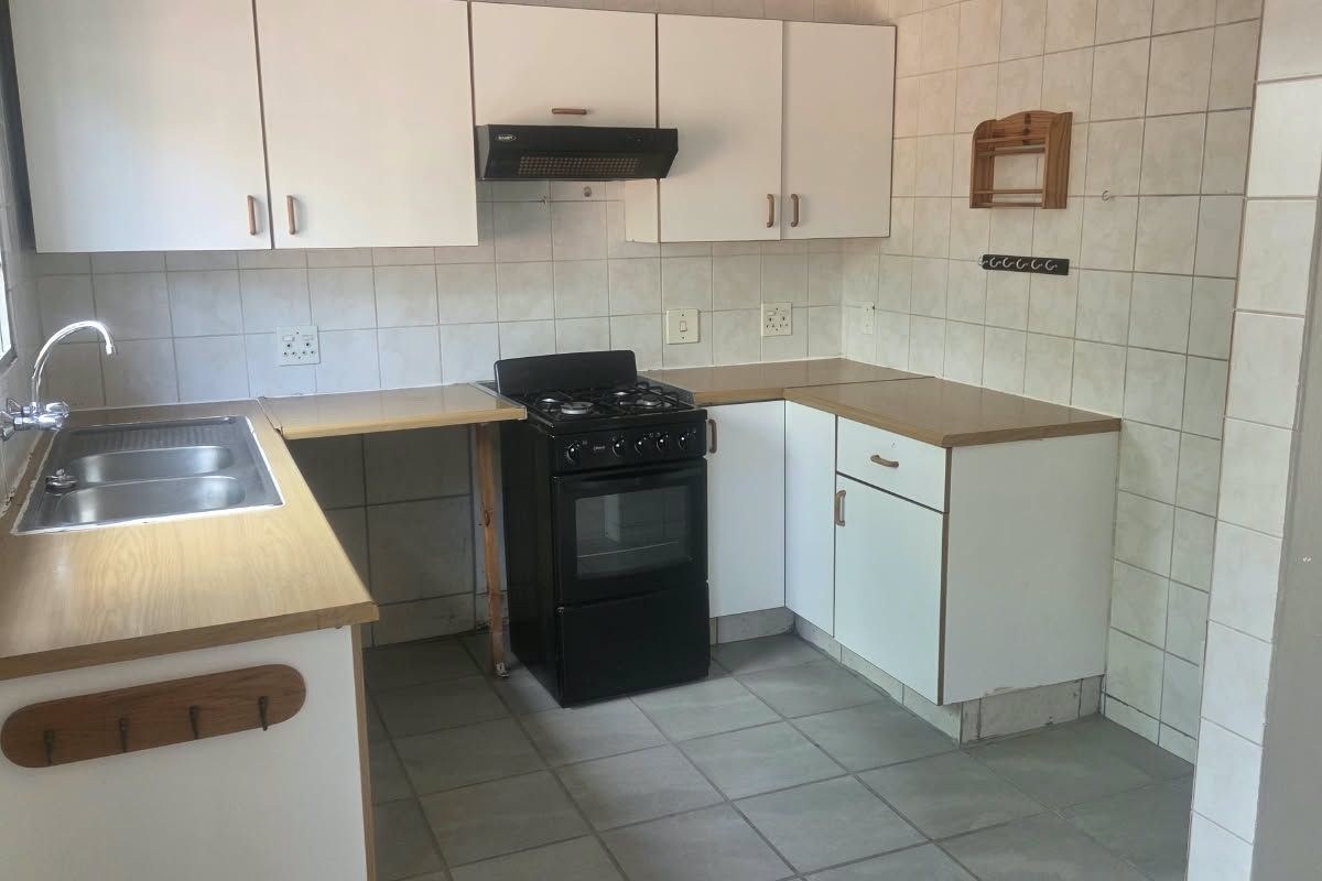 A functional kitchen featuring white cabinetry, laminate countertops, a stainless steel sink, and a freestanding stove with an extractor fan.